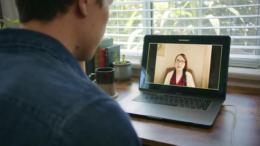 A man sits at a desk with a laptop having a video call
