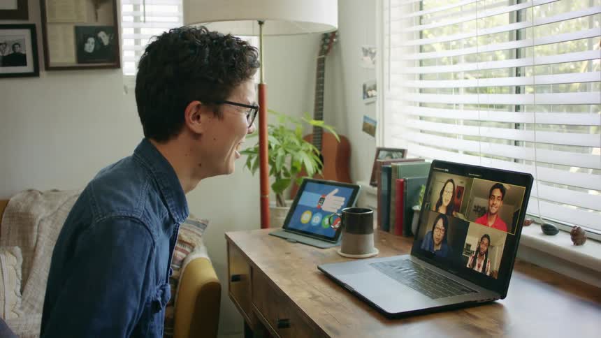 A young man laughs as he participates in a video conference on a laptop