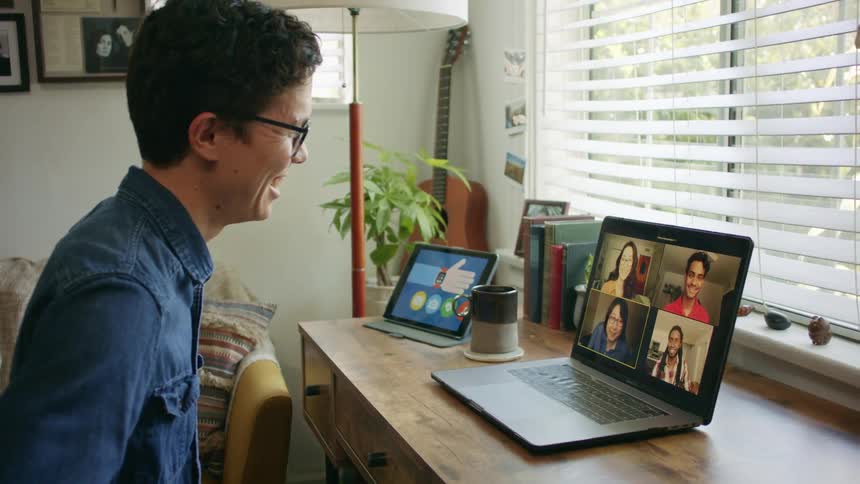 A young man at home video chats with four people on his laptop