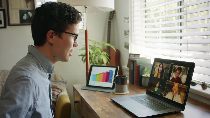 Man with glasses and a blue shirt makes make a group video call on his laptop