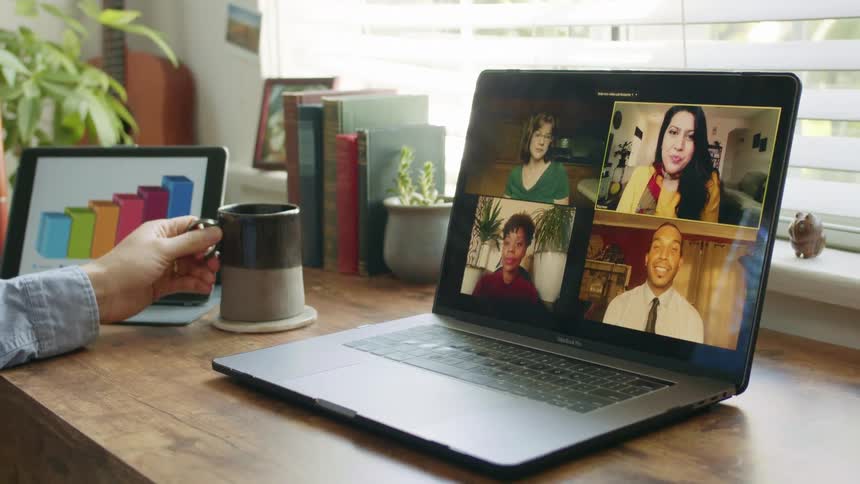 A man at his desk video chats with people on a laptop