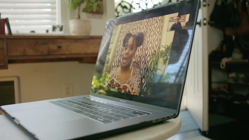 A laptop sitting inside a home with two people on the screen video chatting