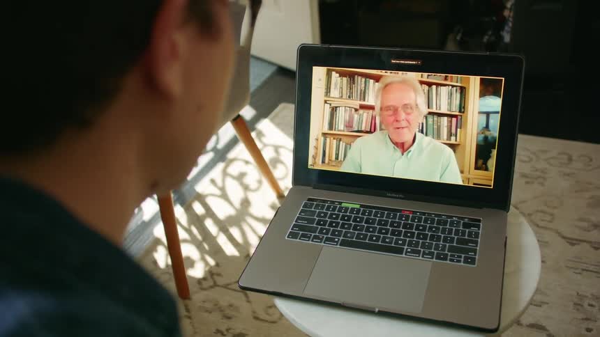 A young man at home video chats with an elderly man on a laptop