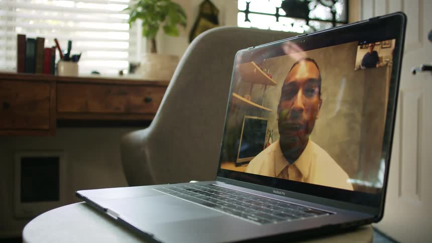 A laptop sitting on a table in a home with a man waving at another man as they video chat