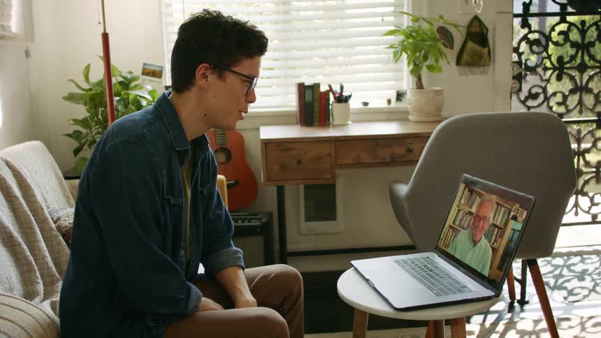 Man with glasses sits and makes a video call on macbook pro with an elderly man in the living room at home