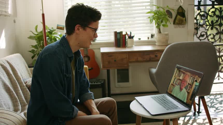 Young man sitting in the living room at home talks to his father on a laptop video call