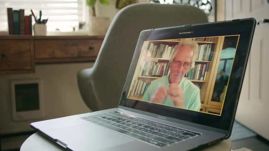 A laptop in a home with an elderly man on the screen talking