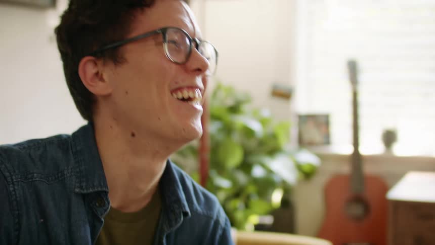 A young man talks and laughs while sitting indoors during the day