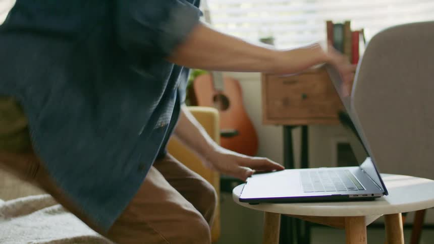 A man closes his laptop and gets up from the couch