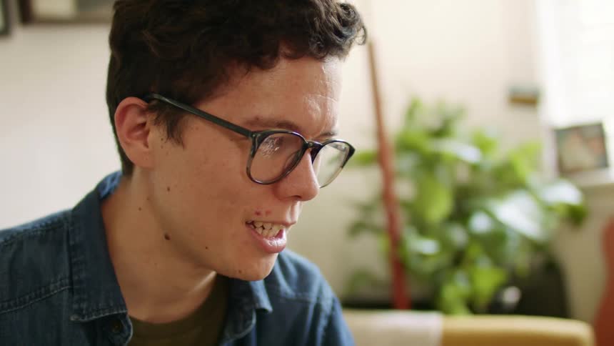 Young man wearing glasses talks on a video call sitting in a couch in the living room