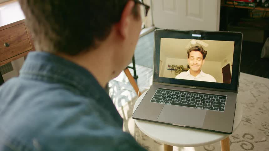 A young man uses his laptop to talk with another young man over video chat