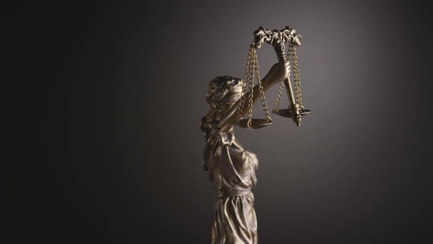 Small figurine of justice holding scales turns in front of camera