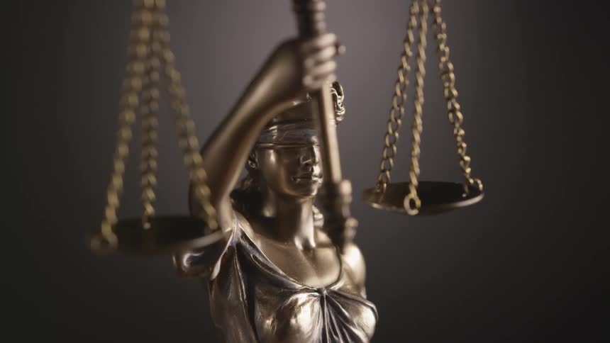 A statute of lady justice holding a scale and blindfolded with a wall in the background