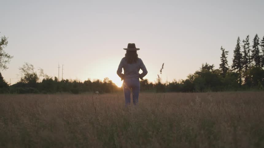 A woman standing in a field of grass watches the sunset