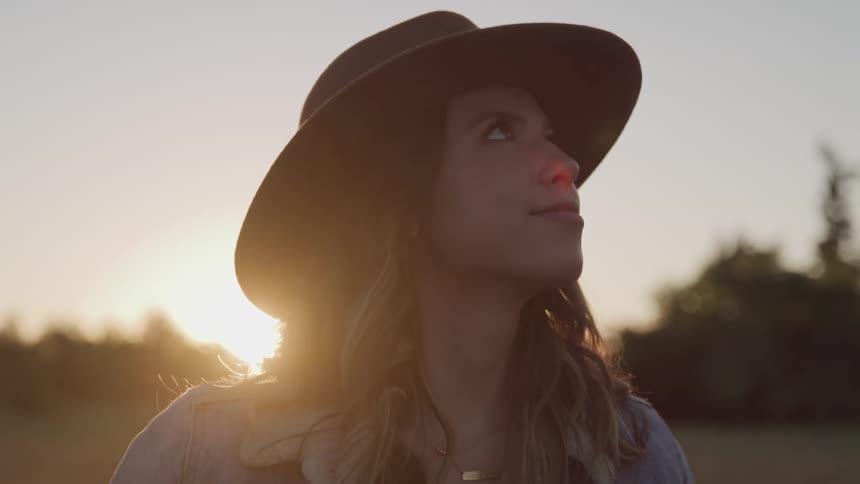 A woman is standing outdoors while wearing a hat at dusk