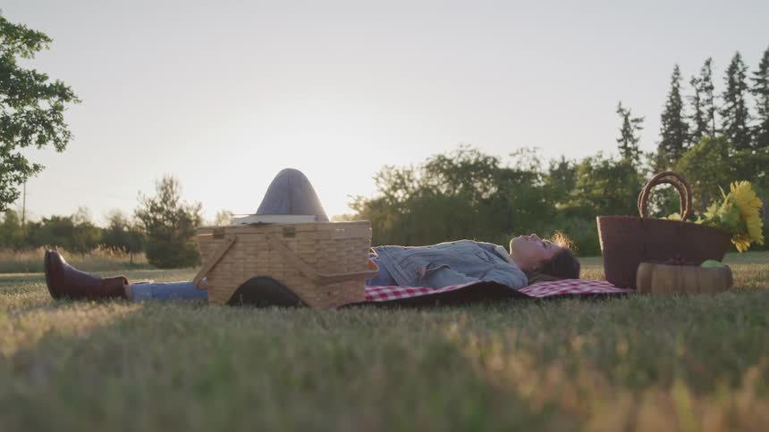 A young woman rests in a field facing the sky on a picnic blanket on a sunny day