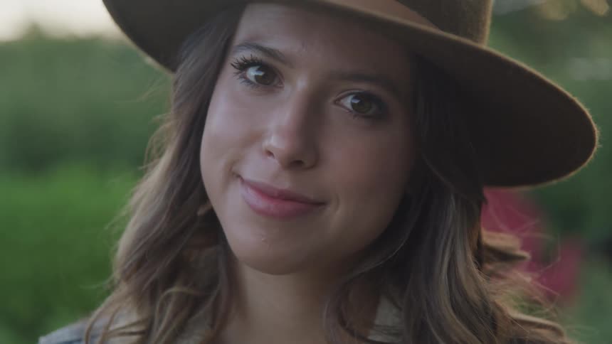 Woman with a brown hat and hair faces the camera smilingly with eye contact