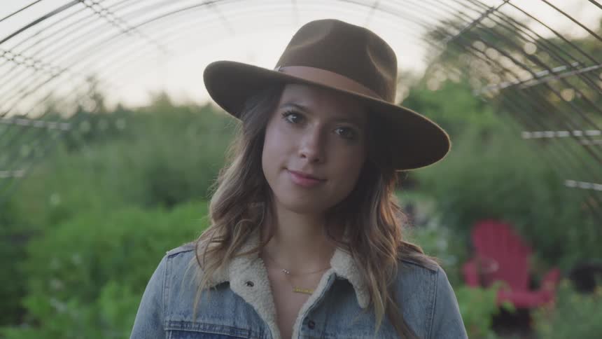 A woman with a hat and jacket smiling in a garden