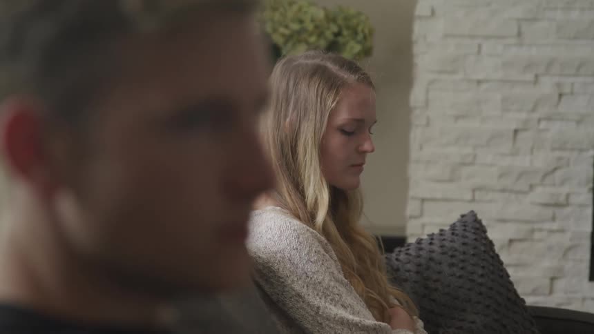 A man and woman sit upset on a couch next to each other