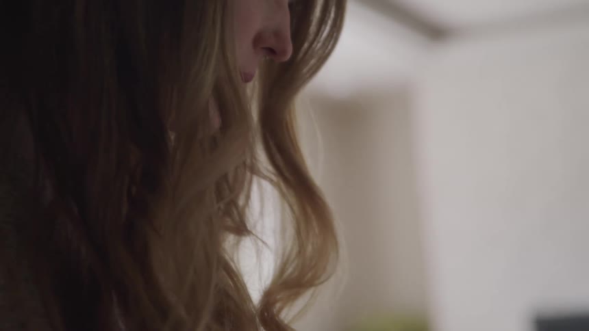 Side view of a woman with brown wavy hair looking down in a room