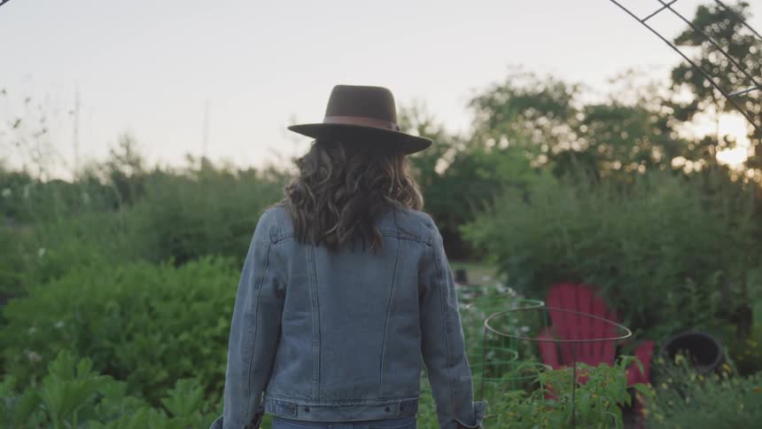 A woman walks pass wire trellises and planters in a garden in the evening