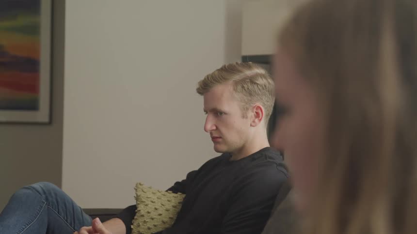 A teenage girl and boy sit far apart from one another on a couch and turn their heads and look at one another in anger