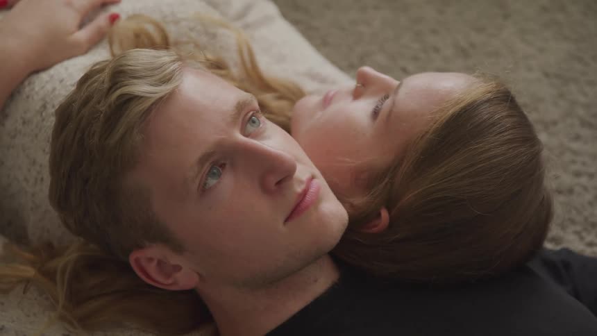 Young couple laying on the rug in the floor with their heads reclined on each other shoulders