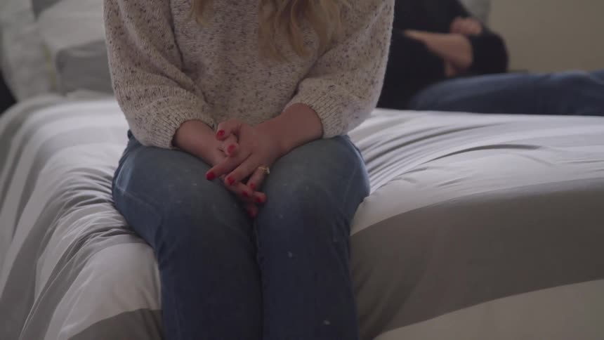Woman nervously sitting on edge of bed with hands together on lap