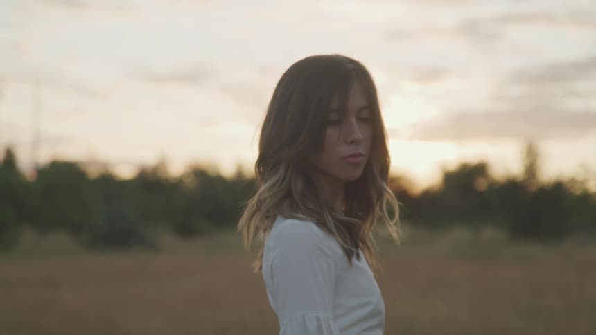Young woman standing on a field at sunset turns around to look at the camera