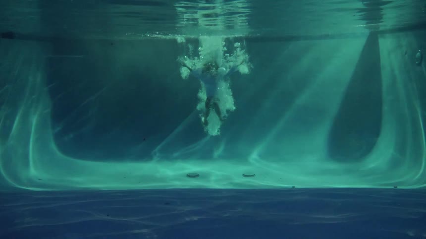 A woman diving in a pool and swimming underwater with bubbles