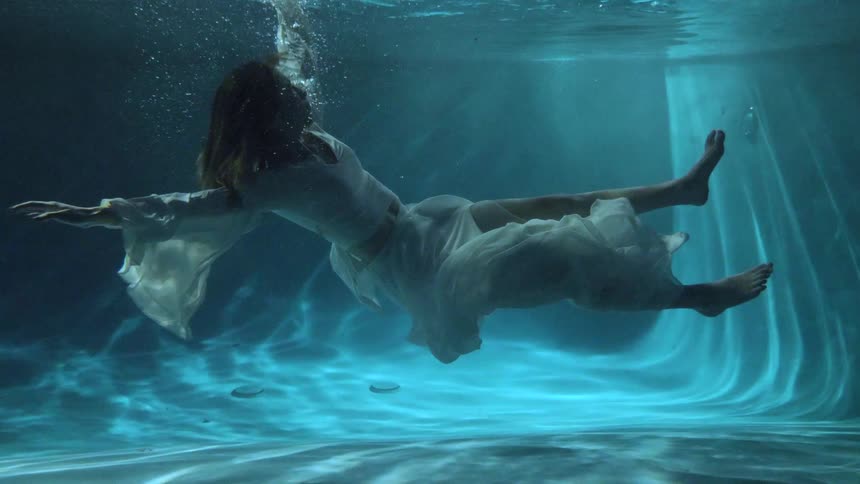 A woman with a white dress floating underwater with bubbles
