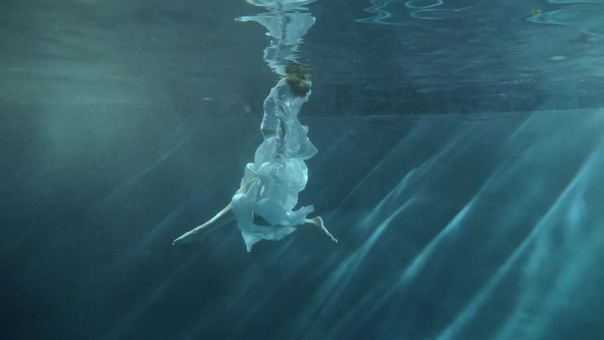 A woman in white flowing clothing swims at the surface of a pool