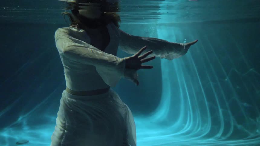A woman dances while standing in a pool with only her head above the surface