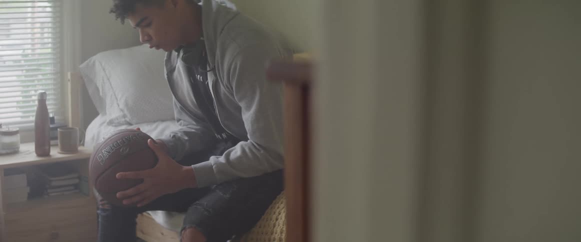 Young man holds a basketball while sitting in the bed at home