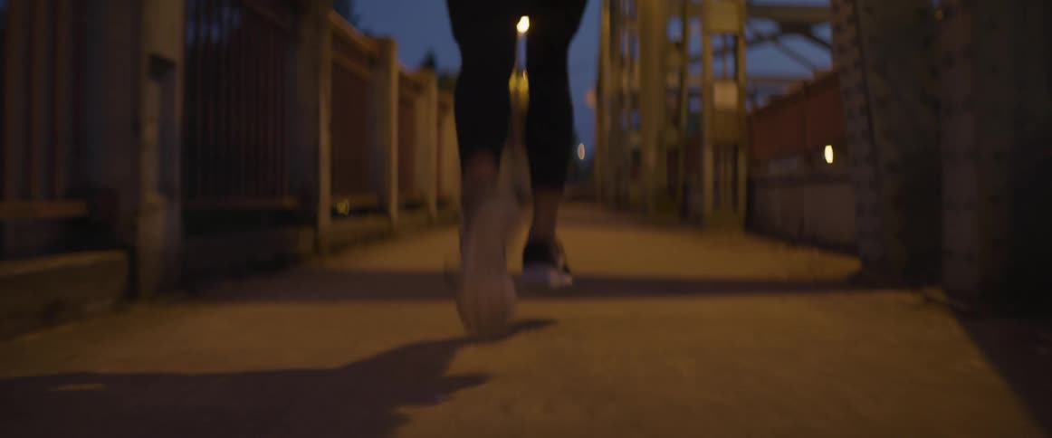 Woman wearing sports clothes jogs on a bridge at night