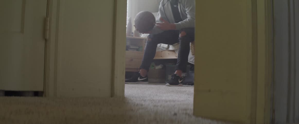 A male sits on a bed and dribbles a basketball in his hands back and forth