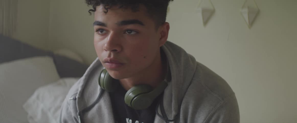 A young boy with headphones around his neck sits at home