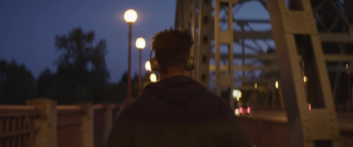 A man jogs across the walkway on a bridge while listening to headphones at night