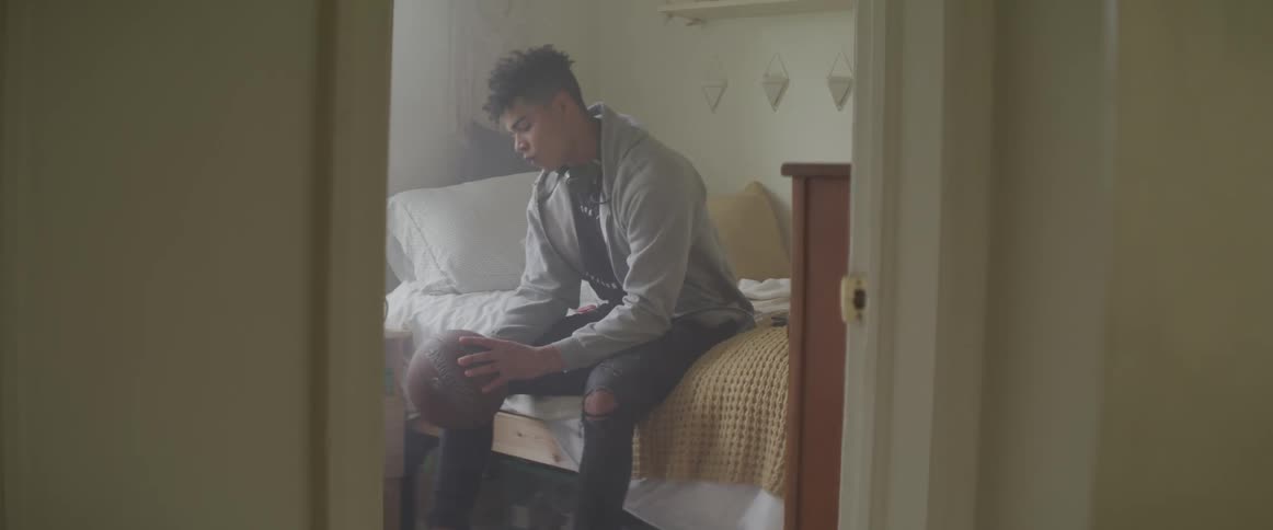 A teenage boy sits on his bed holding a basketball
