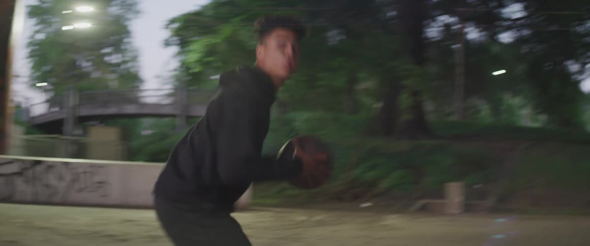 A young male dribbles a basketball and attempts a shot in an outdoor public space