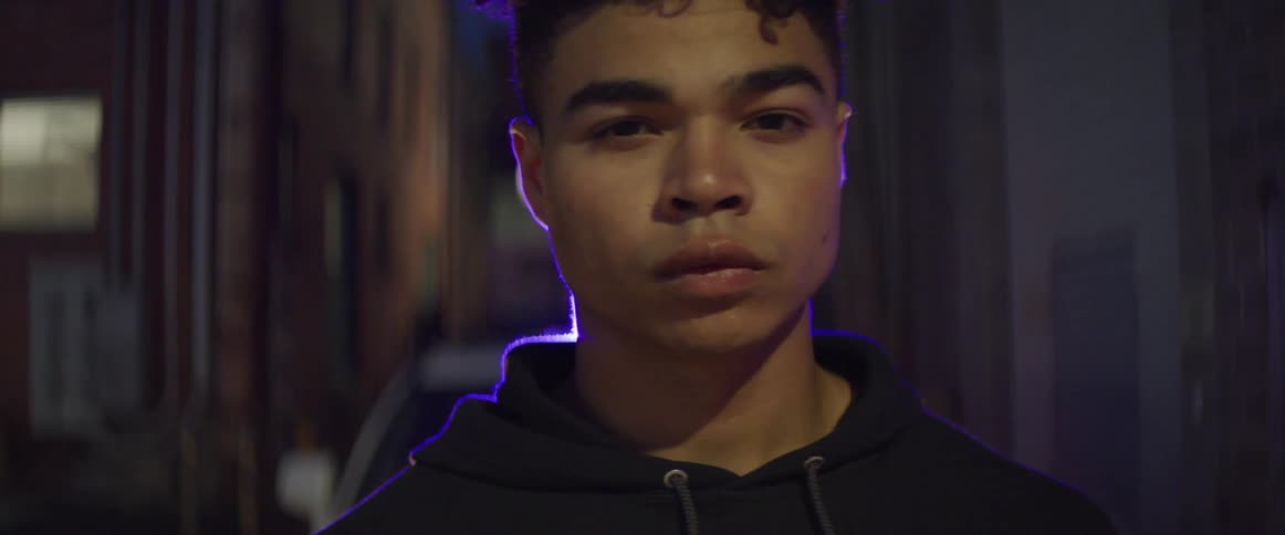 Black teenage boy in front of police car with lights on in alley at night