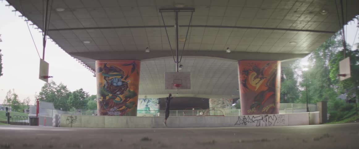 Young man plays basketball in a court under a bridge