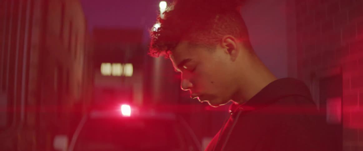 Young man stands in an alleyway in front of the strobing lights of a police car