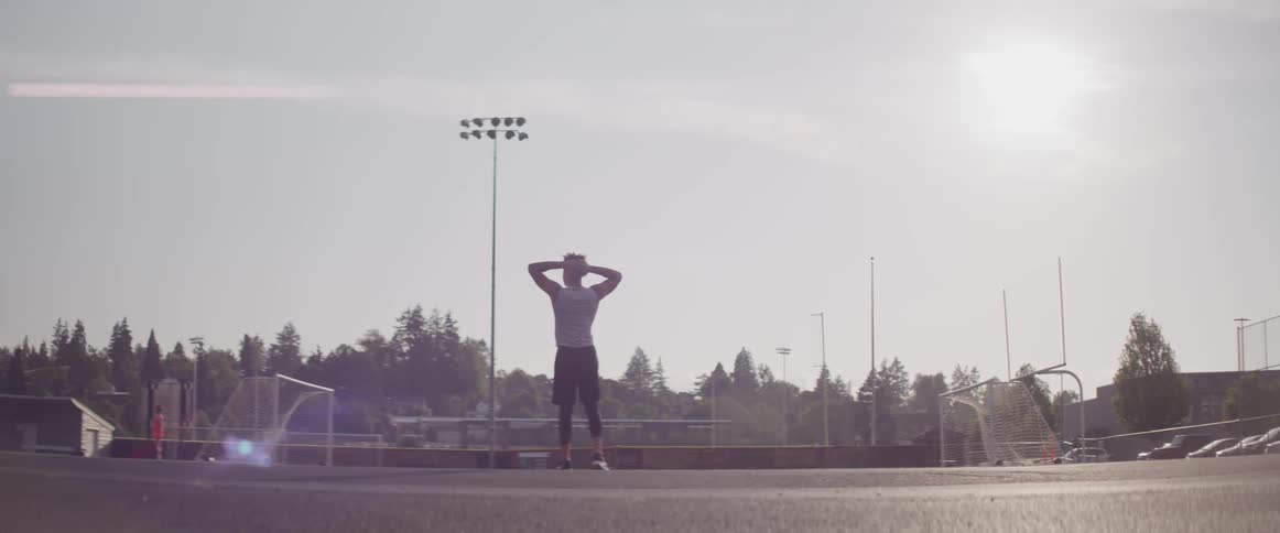 A man shuffles his feet and stands with his hands behind his head on a track while working out