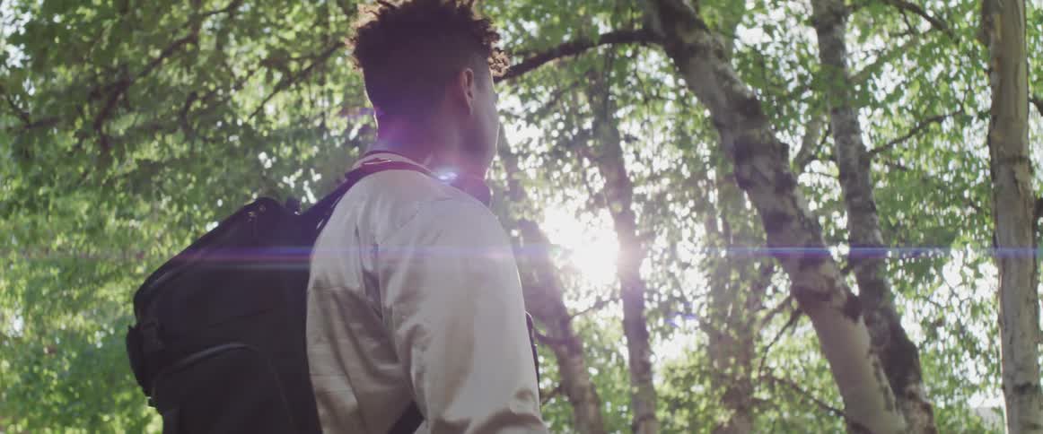 Man wearing backpack and tossing and catching basketball walks past trees on sunny day