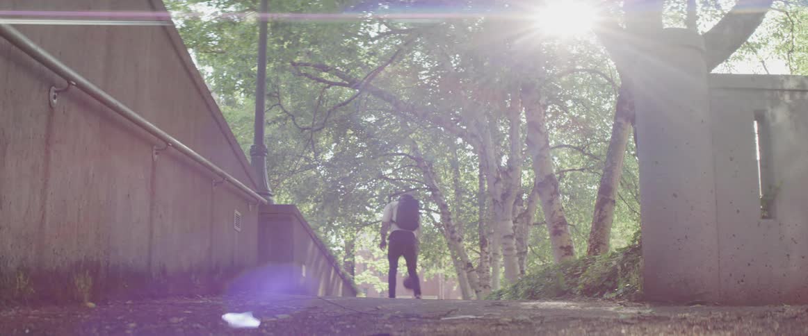 A young man bounces a basketball through a shaded pathway