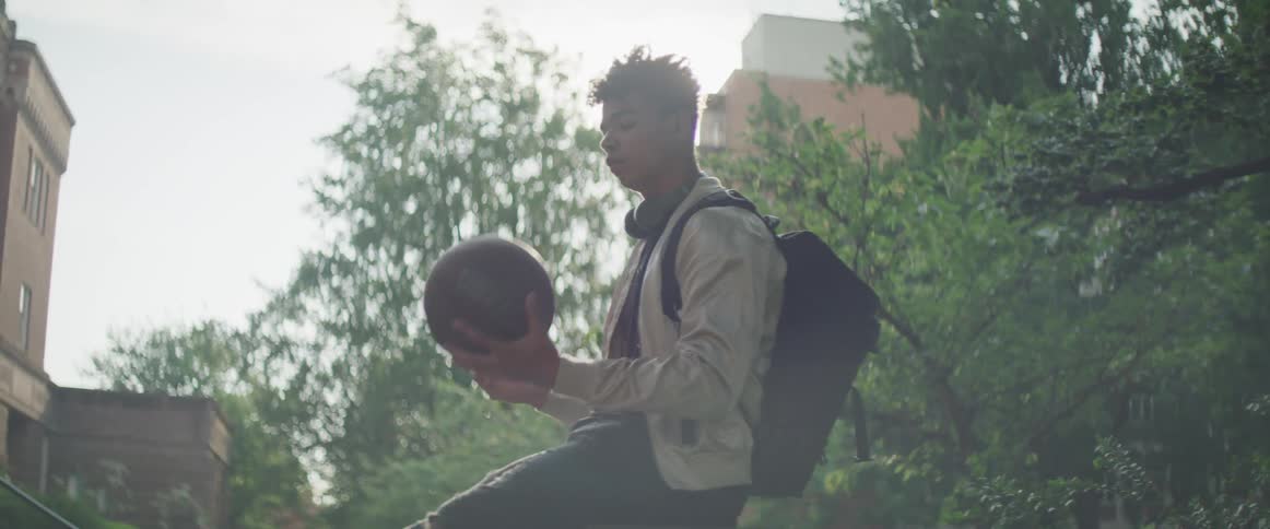 A young man plays with a basketball while sitting on a wall outdoors during the day