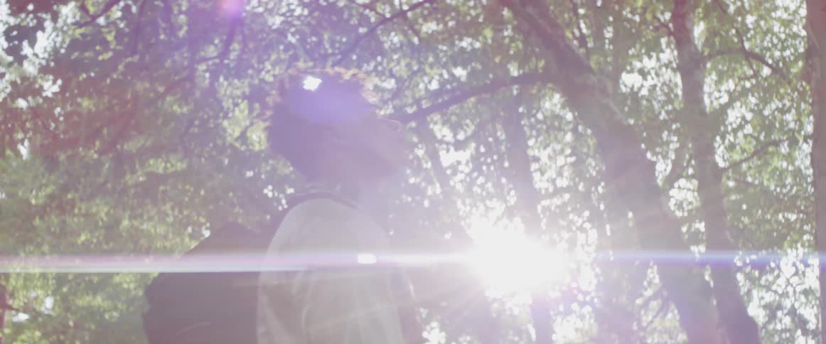 Young man wearing a backpack plays with a basketball next to the trees