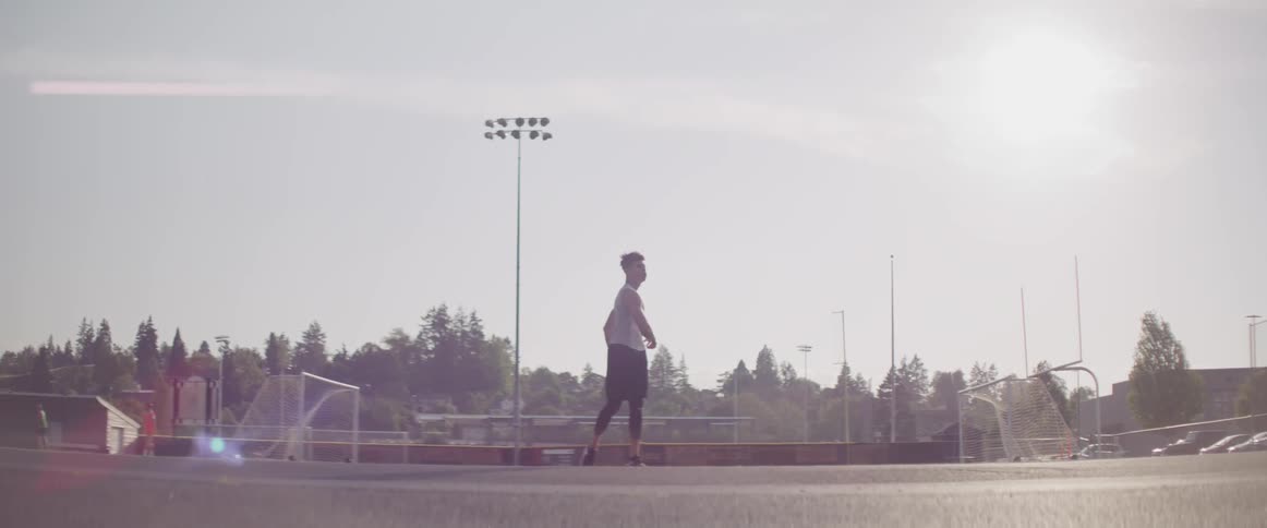 A young man does warm up exercises on an athletics field during the day