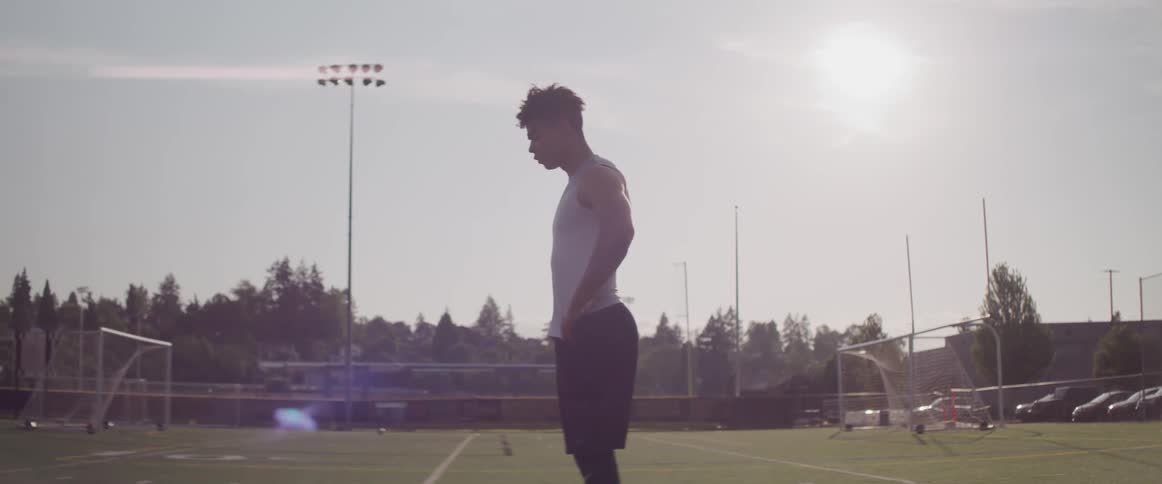 A teenage athlete stands on a soccer field looking tired